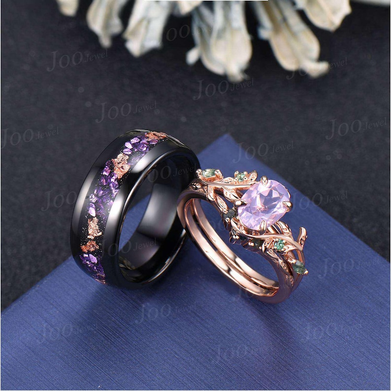 Puede incluir: Una alianza de boda negra con detalles morados y dorados junto a un anillo de compromiso de oro rosa. El anillo de compromiso presenta una piedra preciosa ovalada de color p&uacute;rpura claro y detalles verdes, con un dise&ntilde;o floral.