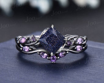 May include: A two-piece ring set featuring a dark blue square gemstone center stone with a speckled appearance. The rings have a silver-colored band with purple accent stones and leaf-like designs. The rings are on a blue surface.