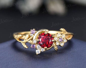 Könnte beinhalten: Ein goldfarbener Ring mit einem großen, runden, roten Edelstein im Zentrum. Der Ring ist mit floralen und Blattmotiven sowie kleineren weißen und lila Edelsteinen verziert. Das Design ist filigran und von der Natur inspiriert.