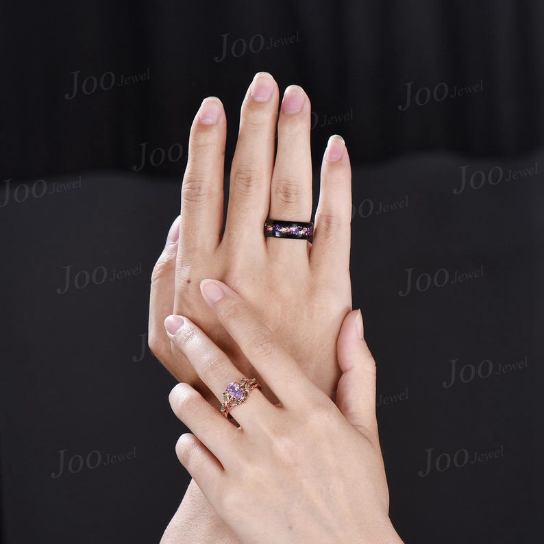 Puede incluir: Dos manos mostrando anillos. Una mano presenta un anillo dorado con una gema p&uacute;rpura y detalles intrincados. La otra mano muestra un anillo negro con un dise&ntilde;o de galaxia en p&uacute;rpura, azul y dorado.