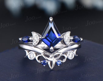 Op de afbeelding: Een zilveren ring met een grote, vierkante blauwe saffier die omringd is door kleinere diamanten. De band is versierd met een halve maan ontwerp en kleinere blauwe saffieren.