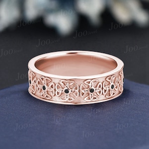 Puede incluir: Una banda de oro rosa con un diseño de nudo celta y diamantes negros. La banda es texturizada y tiene un acabado pulido.