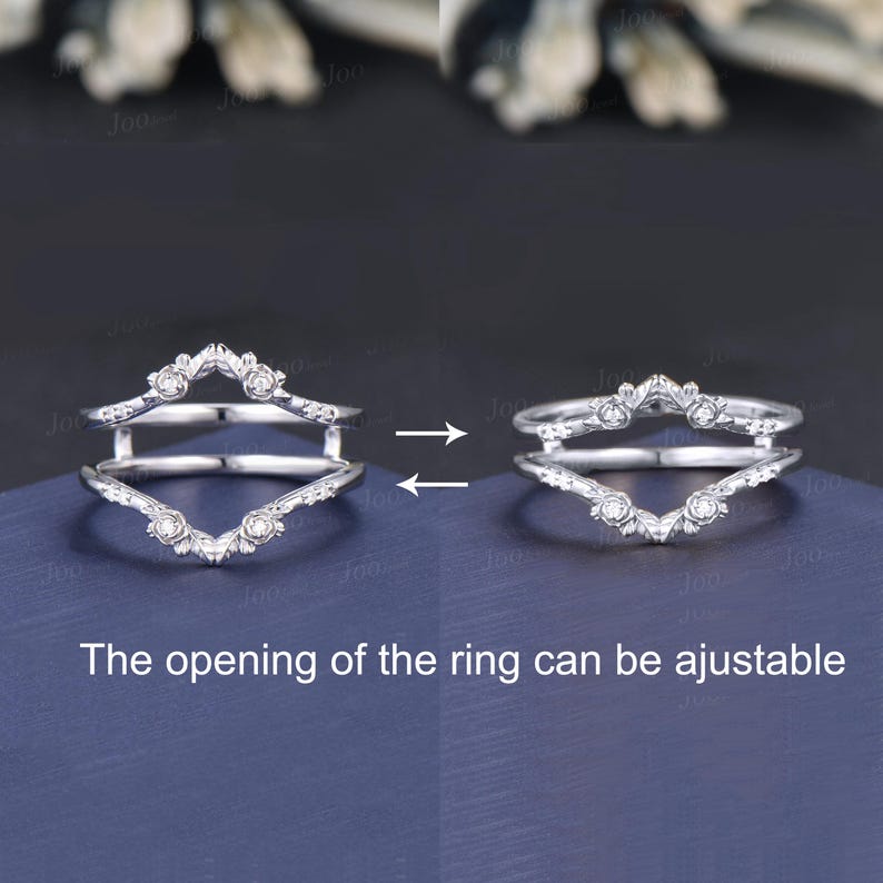 May include: A silver ring guard with a floral design and small clear stones. The ring guard has a V-shaped design and is shown in two positions, with the text "The opening of the ring can be ajustable".