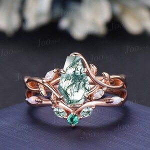 May include: A rose gold engagement ring set with a moss agate gemstone, emerald accents, and opal accents. The ring features a delicate, leafy design.