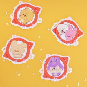 Puede incluir: Cuatro pegatinas de dibujos animados con adorables personajes de animales. Las pegatinas tienen un borde blanco y están sobre un fondo amarillo con confeti en forma de estrella. Cada pegatina tiene un diseño circular rojo y blanco.
