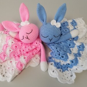 May include: Two crocheted bunny baby blankets, one pink and one blue, with white crocheted trim and a white bow on each bunny's head.