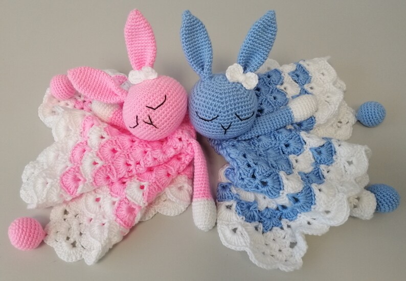 May include: Two crocheted bunny baby blankets, one pink and one blue, with white crocheted trim and a white bow on each bunny's head.