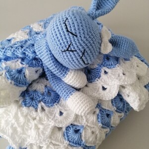 May include: A blue crocheted bunny with a white bow, lying on a blue and white crocheted blanket.