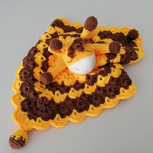 May include: A crocheted baby blanket with a yellow and brown pattern and a small crocheted giraffe attached.