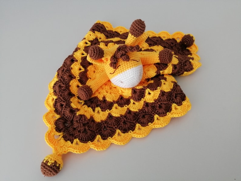 May include: A crocheted baby blanket with a yellow and brown pattern and a small crocheted giraffe attached.