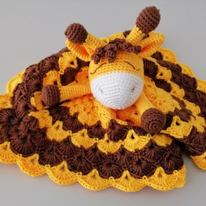 May include: A crocheted giraffe security blanket with brown and yellow stripes. The giraffe has a white face and brown spots. The blanket has a scalloped edge.