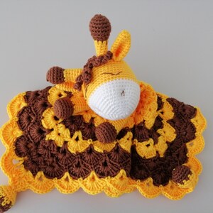 May include: A crocheted giraffe lovey with a brown and yellow blanket. The giraffe has a white face and brown eyes.