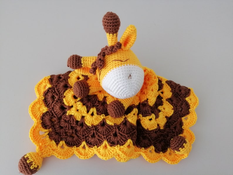 May include: A crocheted giraffe lovey with a brown and yellow blanket. The giraffe has a white face and brown eyes.