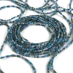 Op de afbeelding: Een kralen tailleketting gemaakt van blauwe, groene en paarse kralen. De ketting is gemaakt van meerdere strengen kralen en is opgerold op een wit oppervlak.