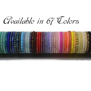 Könnte beinhalten: Eine Sammlung von Perlenarmbändern in verschiedenen Farben, präsentiert auf einem Holzstab. Die Armbänder bestehen aus kleinen, gleichmäßigen Perlen, die ein Spektrum von Grüntönen bis Schwarz zeigen. Text: "Available in 67 Colors."