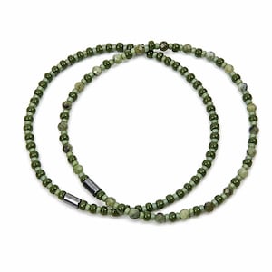 May include: Two olive green beaded necklaces. The necklaces are composed of small, round beads in varying shades of green, with a few faceted beads interspersed. Each necklace has a dark gray, rectangular clasp.
