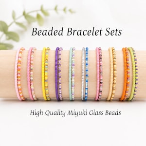 Könnte beinhalten: Eine Sammlung von Armbandsets aus hochwertigen Miyuki-Glasperlen in verschiedenen Farben wie Pink, Gelb, Lila, Mint, Blau und Orange, präsentiert auf einem Holzzylinder mit dem Text Beaded Bracelet Sets und High Quality Miyuki Glass Beads.