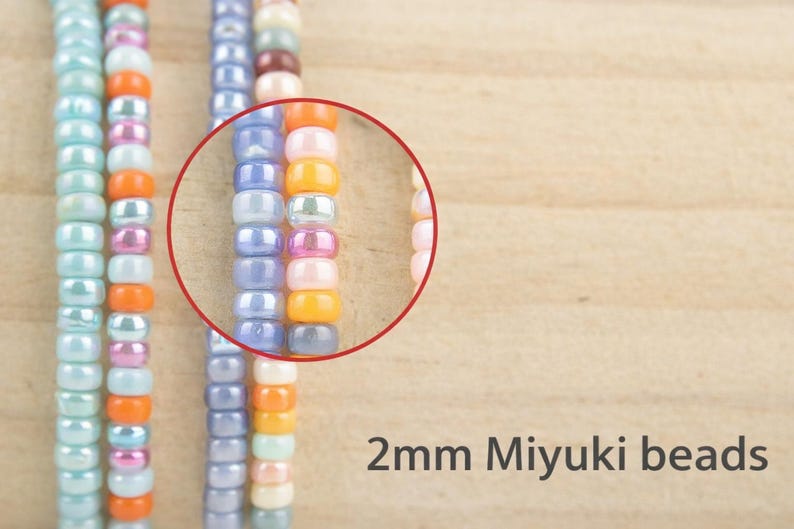 K&ouml;nnte beinhalten: Str&auml;nge aus 2mm Miyuki-Perlen in verschiedenen Farben wie Hellblau, Orange, Pink und Violett. Ein roter kreisf&ouml;rmiger Umriss hebt einen Abschnitt der Perlen hervor und zeigt ihre zylindrische Form und gl&auml;nzende Oberfl&auml;che. Der Text 2mm Miyuki beads ist sichtbar.