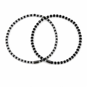 May include: Two circular beaded bracelets featuring an alternating pattern of small, round, glossy black beads and metallic silver-toned beads. Each bracelet is finished with a smooth, cylindrical dark grey metal clasp at the point of closure.