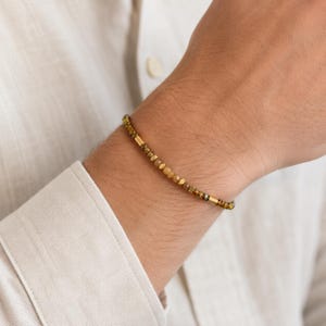 Könnte beinhalten: Ein zartes Armband mit einer Abfolge kleiner, facettierter bernsteinfarbener Perlen, die mit glatten, zylindrischen goldfarbenen Metallzwischenstücken durchsetzt sind. Die Perlen zeigen verschiedene Schattierungen von durchscheinendem Braun und Goldgelb.