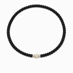Könnte beinhalten: Schwarzes Perlenarmband mit einer einzelnen, hellfarbigen Mittelperle. Das Armband besteht aus kleinen, runden schwarzen Perlen, die aufgereiht sind, mit einer kontrastierenden hellen Perle in der Mitte, zwischen silberfarbenen Abstandshaltern.