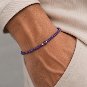 Op de afbeelding: Een paarse kralenarmband met een zilveren accentkraal. De armband is gemaakt van kleine, ronde kralen en wordt om de pols gedragen. De armband is een eenvoudig en elegant sieraad.