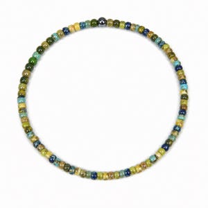 May include: A beaded bracelet featuring small, colorful beads in shades of green, blue, yellow, and brown. The beads are strung together to form a circular shape. A single, dark metallic bead is centered on the bracelet.