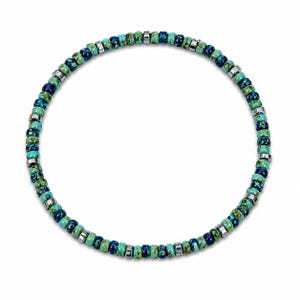 May include: A necklace with a circular design, composed of turquoise, teal, and navy blue beads. Small silver-coloured metal spacers are placed between the beads. The beads have a speckled pattern. The necklace is likely a choker or bracelet.
