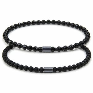 May include: Two black beaded bracelets. One bracelet features faceted beads, the other has matte beads. Both bracelets have a small, rectangular, dark grey accent bead in the centre.