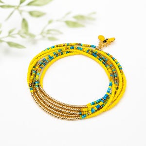 May include: A multi-strand wrap bracelet composed of small yellow, turquoise, and metallic gold beads. The bracelet features a small gold-toned bee charm with black detailing attached to one end, creating a layered circular design.