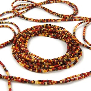 Op de afbeelding: Een meerstrengs kralenketting met rode, oranje, gele en zwarte kralen. De ketting is gemaakt van kleine, ronde kralen en is in een cirkelvormig patroon gerangschikt.