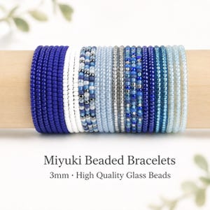 Könnte beinhalten: Eine Sammlung von Miyuki-Perlenarmbändern mit 3mm hochwertigen Glasperlen in einem Farbverlauf aus Blau-, Weiß- und Silbertönen. Der Text lautet: Miyuki Beaded Bracelets, 3mm • High Quality Glass Beads. Die Armbänder sind in einer Reihe angeordnet.