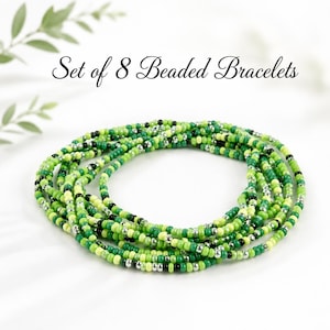 Könnte beinhalten: Ein Set aus 8 Perlenarmbändern, die in einer kreisförmigen Formation angeordnet sind. Die Armbänder bestehen aus kleinen runden Perlen in verschiedenen Grüntönen, darunter Limette, Smaragd und Oliv, durchsetzt mit kleinen silbernen und schwarzen Akzentperlen.