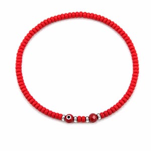 May include: A red beaded bracelet with an evil eye charm and a faceted red bead. The bracelet is made of small, round red beads strung together. The evil eye charm is red with a black pupil and silver accents.