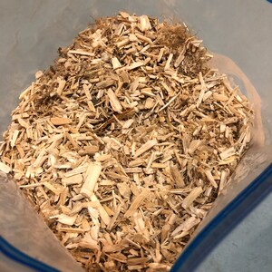 Puede incluir: Una bolsa de pl&aacute;stico llena de virutas de madera. Las virutas son de color marr&oacute;n claro y parecen estar hechas de madera blanda.