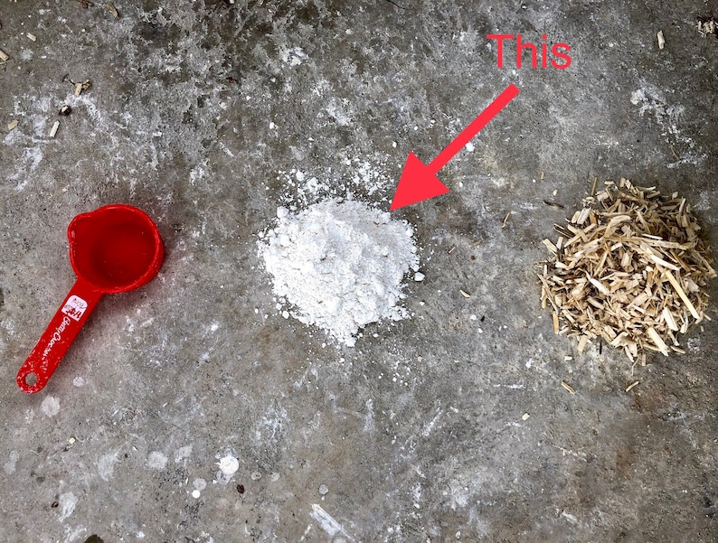 May include: A white powder, a red measuring cup, and wood shavings on a gray concrete surface. The text "This" is written in red above an arrow pointing to the white powder.