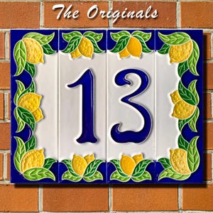 May include: A rectangular house number plaque featuring the number 13 in dark blue on a white background. The border is decorated with yellow lemons and green leaves on a deep blue field. The text The Originals is printed at the top.