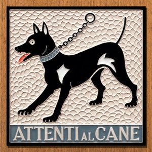 Op de afbeelding: Een zwart-witte keramische tegel met een zwarte hond aan een ketting. De tegel heeft een witte achtergrond met een patroon van overlappende cirkels. De tekst "ATTENTI AL CANE" staat in blauw onderaan de tegel.