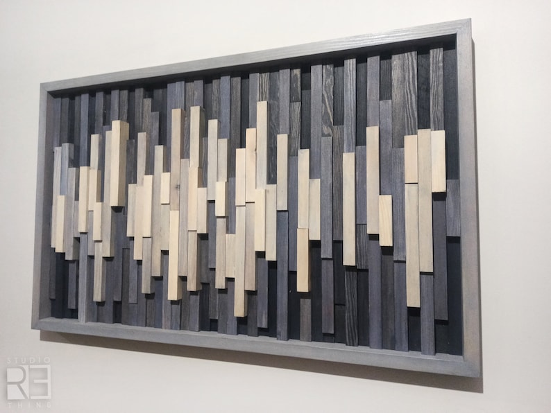 May include: A gray wood wall art piece with a wave-like pattern made of various shades of gray and beige wood pieces. The art is framed in a gray wood frame.