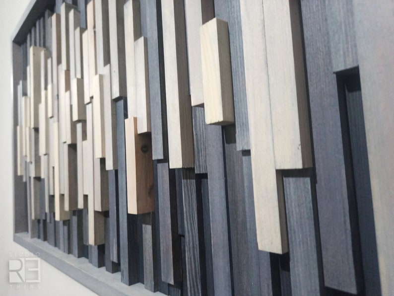 May include: A framed wall art piece made of various wood planks in shades of gray, white, and brown. The planks are arranged in a random pattern, creating a modern and abstract design.