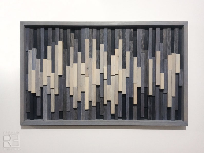 May include: A framed wall art piece made of wood with a wave-like pattern. The wood is stained in shades of gray and white.