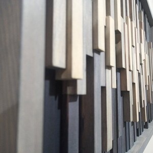 May include: A wall art piece made of various wood pieces in shades of gray, brown, and white. The wood pieces are arranged in a random pattern, creating a modern and abstract design.