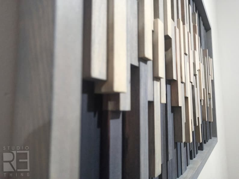 May include: A wall art piece made of various wood pieces in shades of gray, brown, and white. The wood pieces are arranged in a random pattern, creating a modern and abstract design.