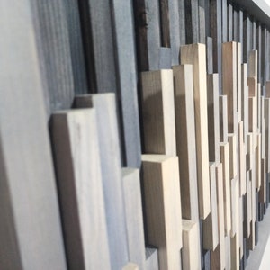 May include: A wall art piece made of various wood pieces in shades of gray, brown, and beige. The wood pieces are arranged in a geometric pattern, creating a modern and abstract design.