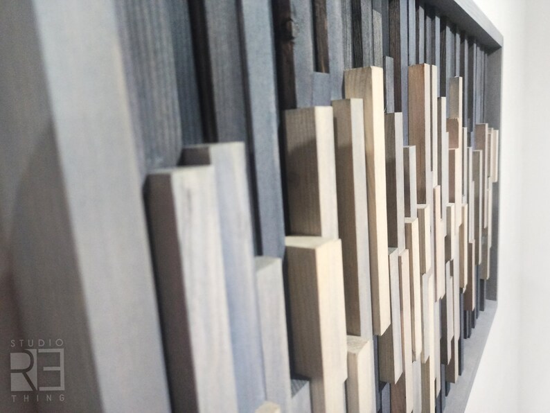 May include: A wall art piece made of various wood pieces in shades of gray, brown, and beige. The wood pieces are arranged in a geometric pattern, creating a modern and abstract design.