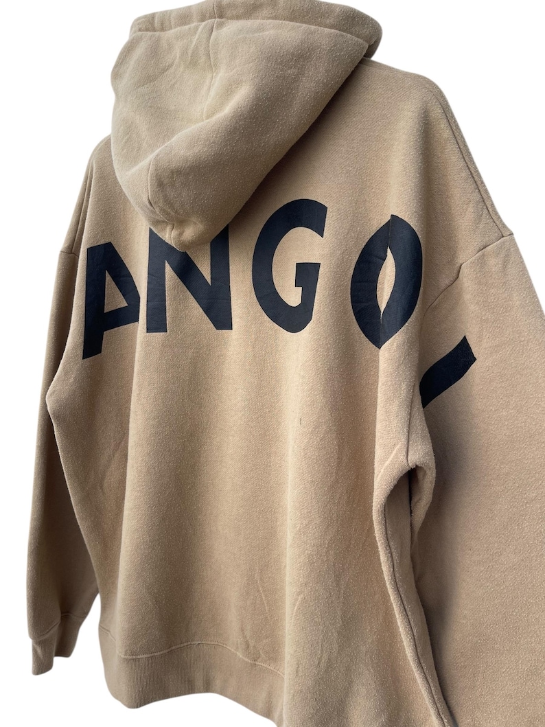 May include: A tan hoodie with a hood and long sleeves. The word "ANGO" is printed in large, black letters across the back of the hoodie. The hoodie is made of a soft, comfortable material.