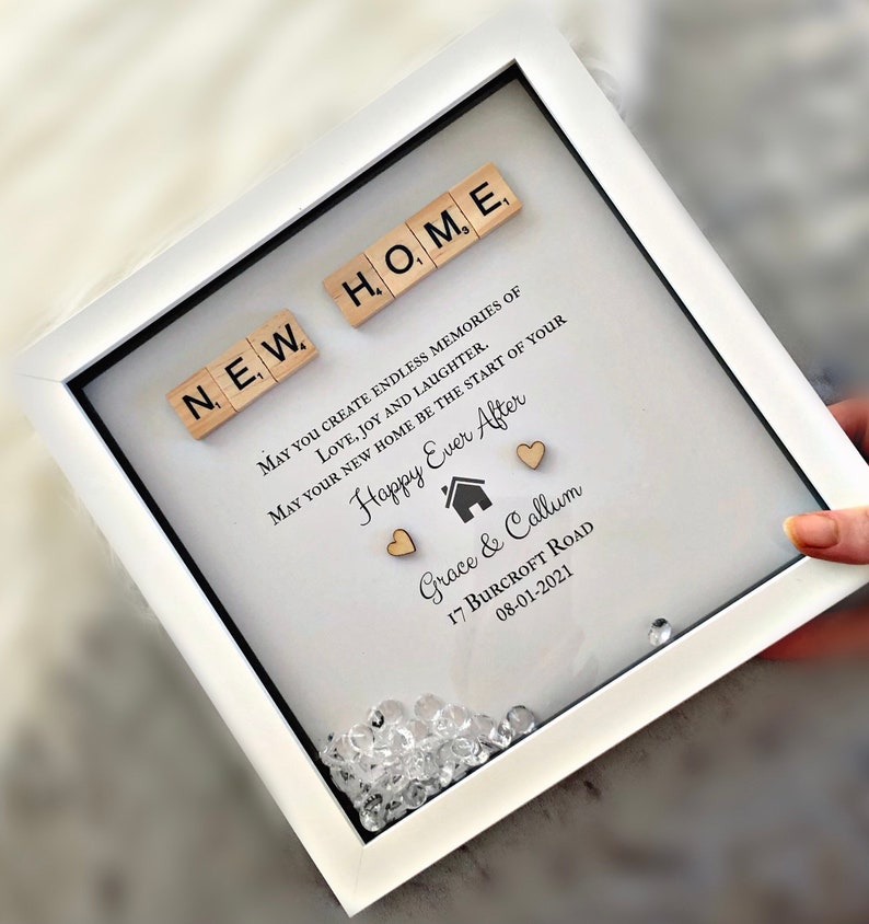 Pu&ograve; includere: Una cornice bianca con un passepartout bianco e un fronte di vetro. La cornice contiene un messaggio che dice "May you create endless memories of love, joy and laughter. May your new home be the start of your Happy Ever After." Il messaggio &egrave; scritto con inchiostro nero ed &egrave; circondato da piccole tessere di legno che compongono la scritta "NEW HOME". Ci sono anche due piccoli cuori di legno e un piccolo simbolo di casa in legno. La parte inferiore della cornice contiene i nomi "Grace & Callum", l'indirizzo "17 Burcroft Road" e la data "08-01-2021".