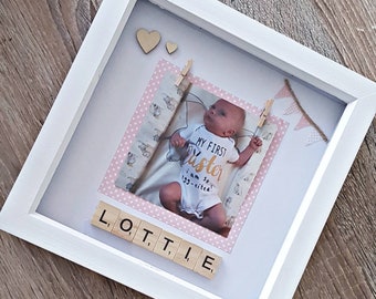 May include: A white picture frame with a pink and white patterned background. A photo of a baby girl wearing a white onesie with the text "My First Sister I am so excited!" is in the frame. The baby's name, "Lottie", is spelled out with wooden letter tiles.