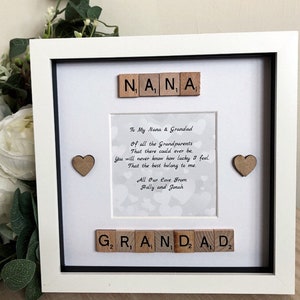 May include: A white picture frame with a black mat and a white background. The frame contains a poem about grandparents, with the words "Nana" and "Grandad" spelled out in wooden letter tiles. The poem reads: "To My Nana & Grandad Of all the Grandparents That there could ever be. You will never know how lucky I feel. That the best belong to me. All Our Love From Holly and Jonah"