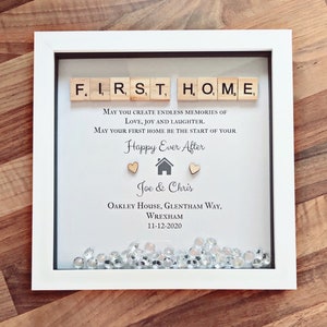 Pu&ograve; includere: Una cornice bianca con un passepartout nero e uno sfondo bianco. La cornice contiene un messaggio che recita "FIRST HOME" scritto con tessere di lettere in legno. Il messaggio continua con "May you create endless memories of love, joy and laughter. May your first home be the start of your Happy Ever After." Il messaggio &egrave; seguito da una piccola icona di casa, due cuori e i nomi "Joe & Chris". I nomi sono seguiti dall'indirizzo "Oakley House, Glentham Way, Wrexham" e dalla data "11-12-2020". La parte inferiore della cornice &egrave; piena di gemme scintillanti e trasparenti.